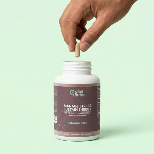 Hand holding a supplement capsule above 'giminutra' ashwagandha bottle on a light green background