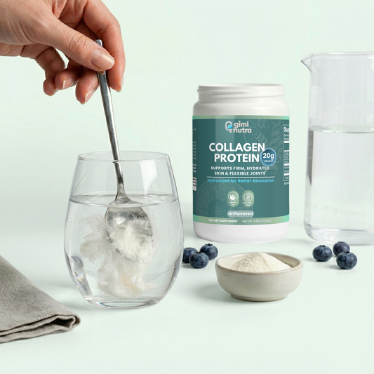 Giminutra collagen protein being stirred into a glass of water with a spoon. The glass is set next to berries and the collagen contain is in the back, on a mint green background.