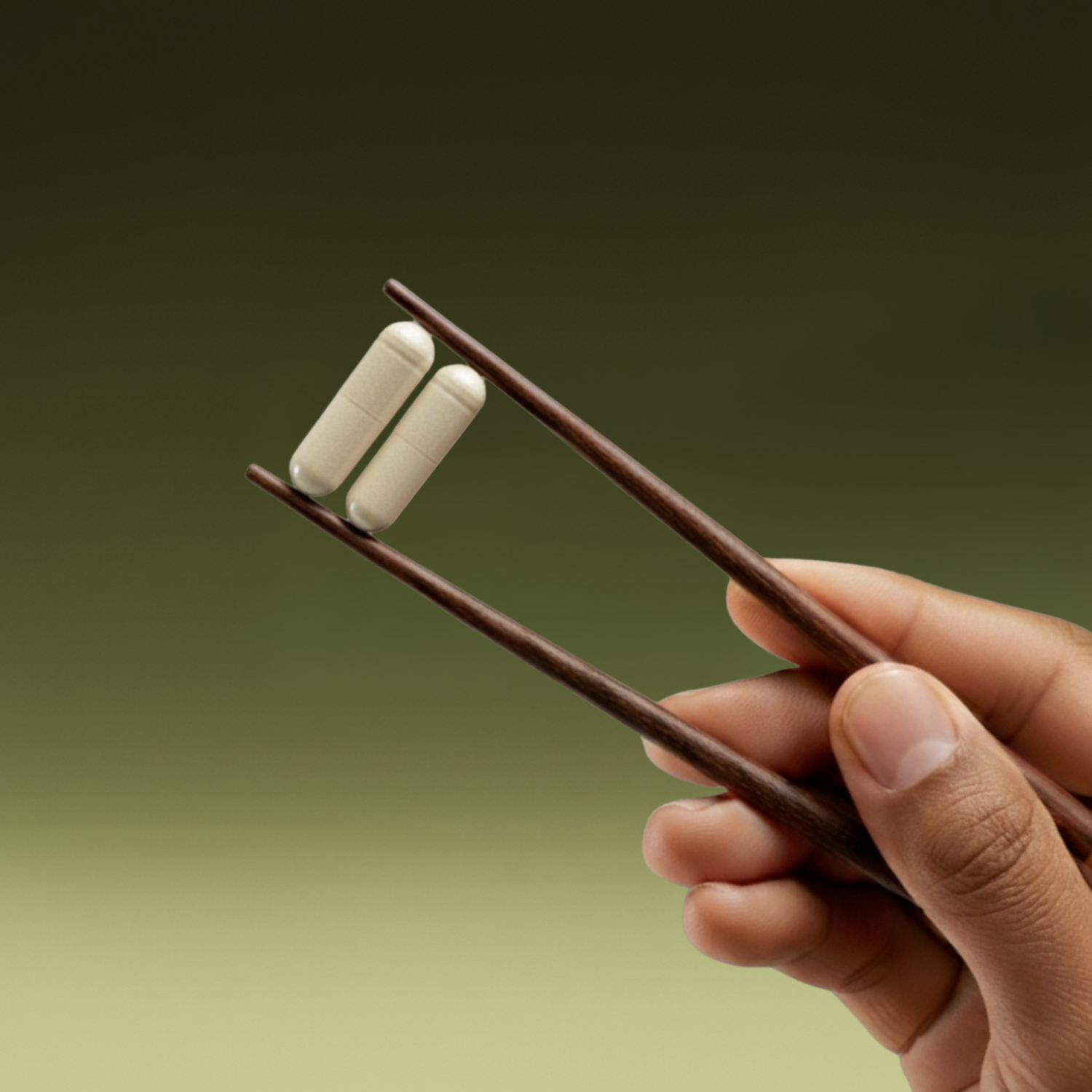 Hand holding pills wedged between brown chopsticks with a green gradient background 