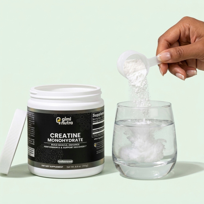 Hand pouring a scoop of creatine powder into a glass of water standing next to a "giminutra" creatine container with the lid off on a soft mint background. 