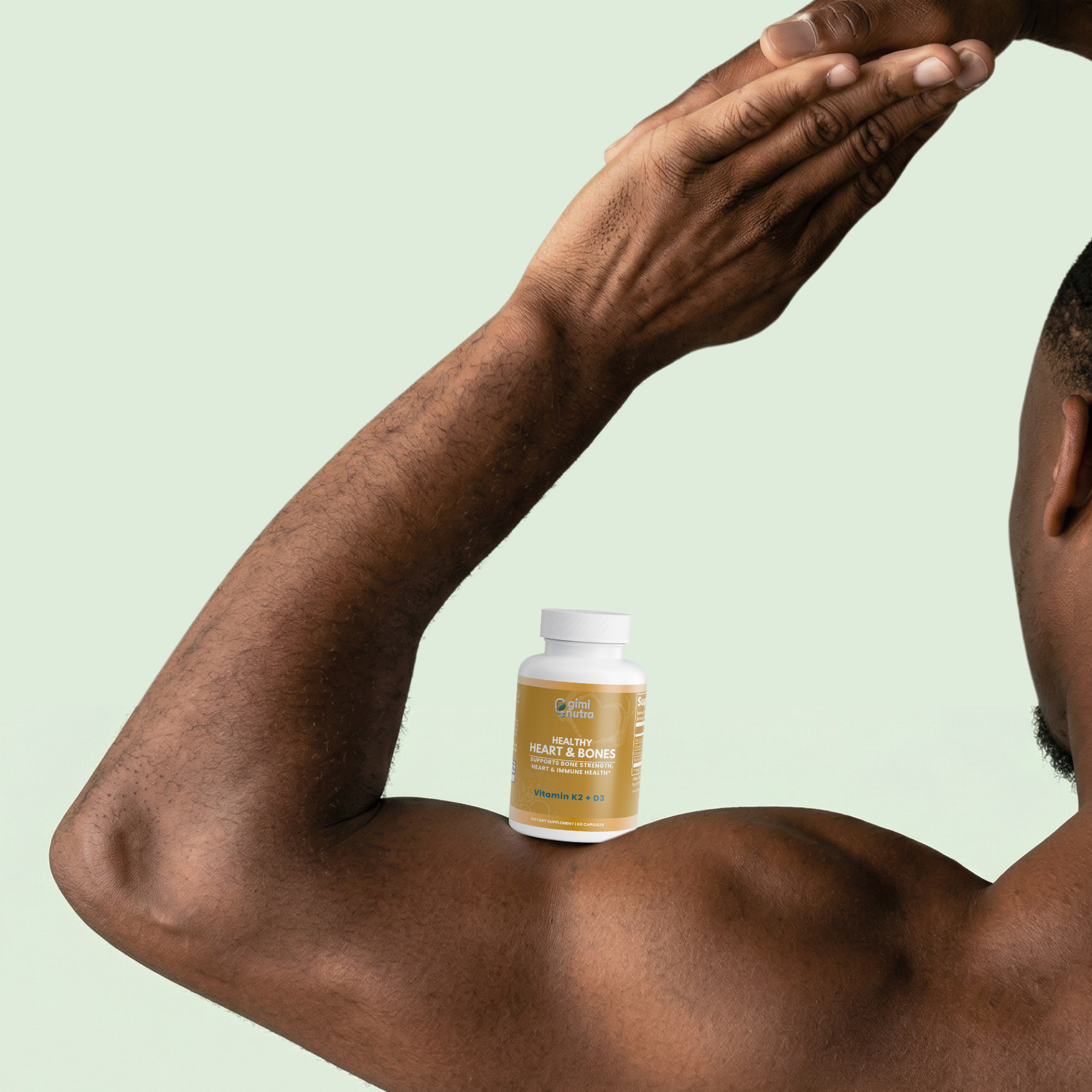 Man with a bottle of giminutra's vitamin K2+D3 supplement on his arm against a mint green background