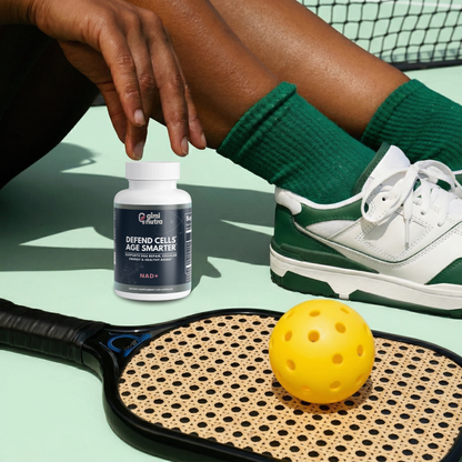 Person sitting on a pickleball court with a giminutra NAD+ supplement bottle and pickleball racket.