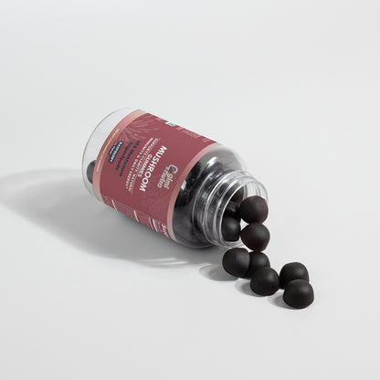 A open bottle of Giminutra's mushroom gummies with gummies spilling out of bottle on a white surface and background