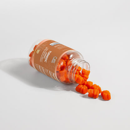 Opened bottle of Giminutra's turmeric gummies with spilled gummies on a white surface on a white background